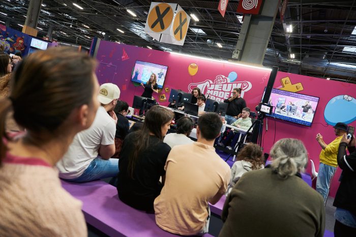 Photo de la finale de la CapGame Arena sur la scène Jeux Made in France.
Quatre joueurs sont entrain de s'affronter sur le jeux vidéo de foot.
Sur la scène il y a deux commentateurs et une interprète en langue des signes française.