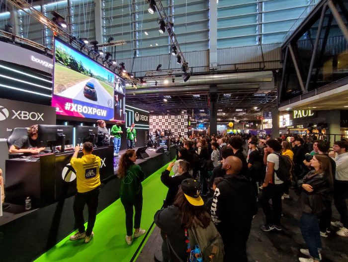 Photo de la finale de la CapGame Arena sur la scène Xbox.
Un joueur est entrain de faire la compétition du jeux vidéo de course de voiture.
Sur la scène il y a deux commentateurs et une interprète en langue des signes française.