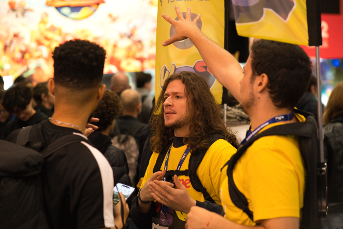 2 membres "volants" de l'équipe access, portant leur sac-drapeau jaune "Comment puis-je vous aider ?", qui renseignent un visiteur au milieu de la foule.